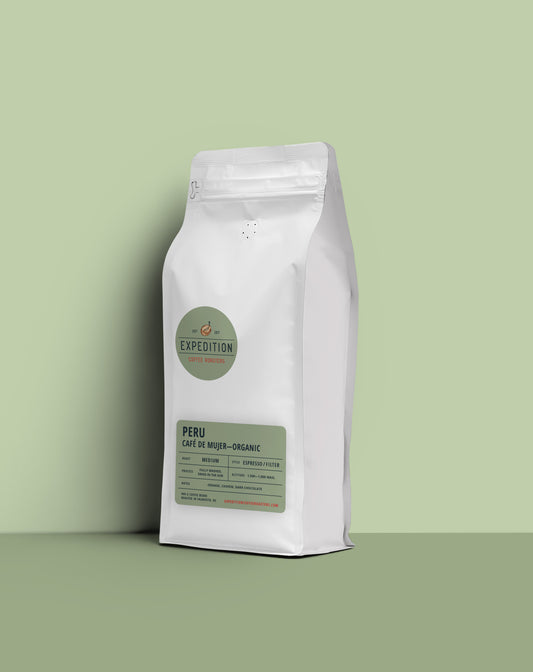 A white stand-up coffee bag labeled Expedition Peru Café de Mujer-Organic, standing on a matching light green surface against a pale green background.